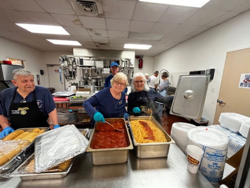3 women on serving line handling pasta, spaghetti and Italian bread