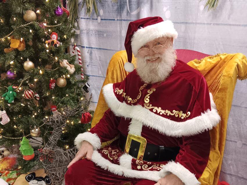 Man in Santa suit next to Christmas tree